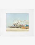 A framed California Print, 'Santa Monica Pier' by Offley Green, depicting a vibrant seaside amusement park with a ferris wheel and roller coaster at Santa Monica Pier, displayed against a clear sky.