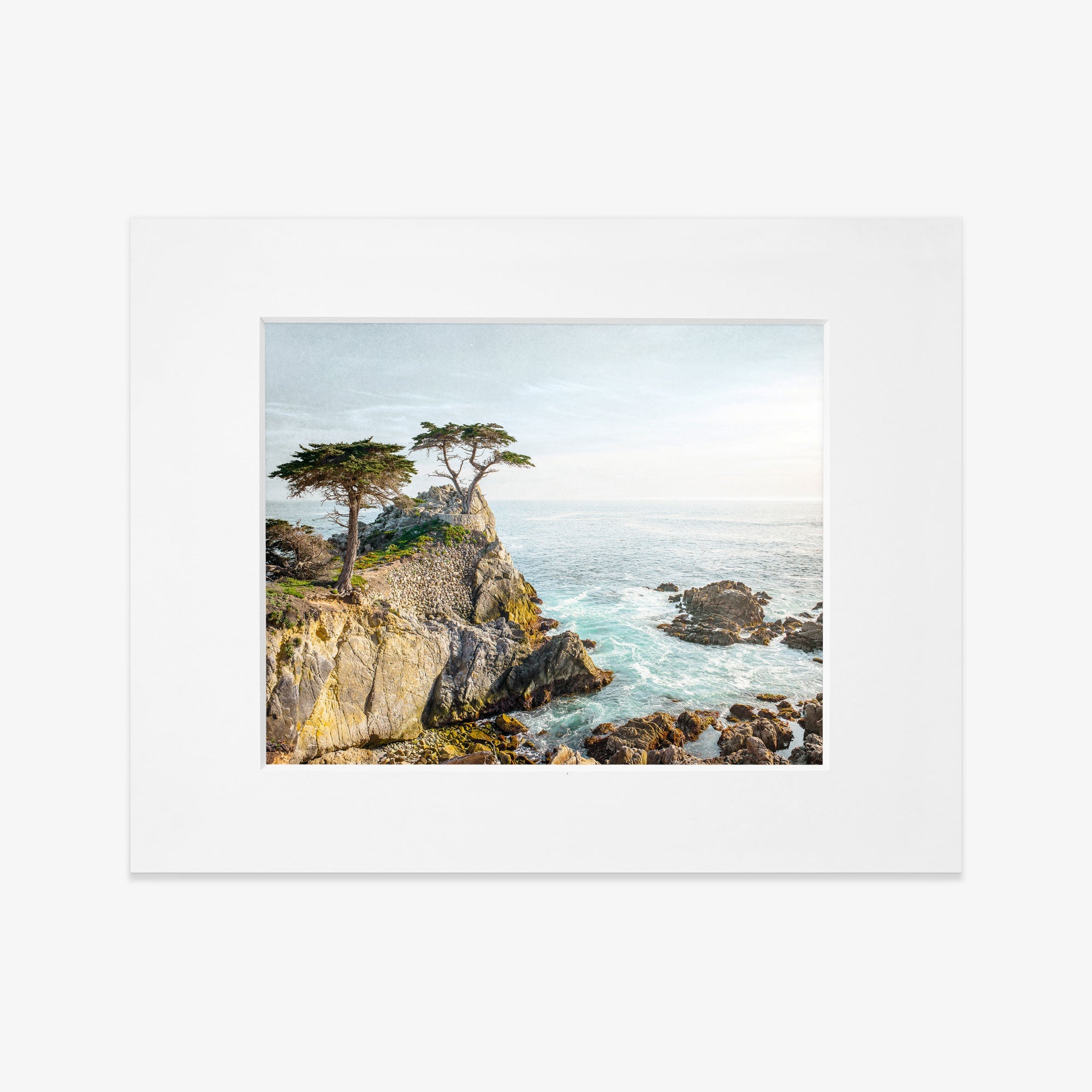 A framed painting of a California Coastal Print, &#39;Lone Cypress&#39; by Offley Green, featuring trees on a rocky cliff overlooking a turbulent sea at Pebble Beach, displayed against a white background.