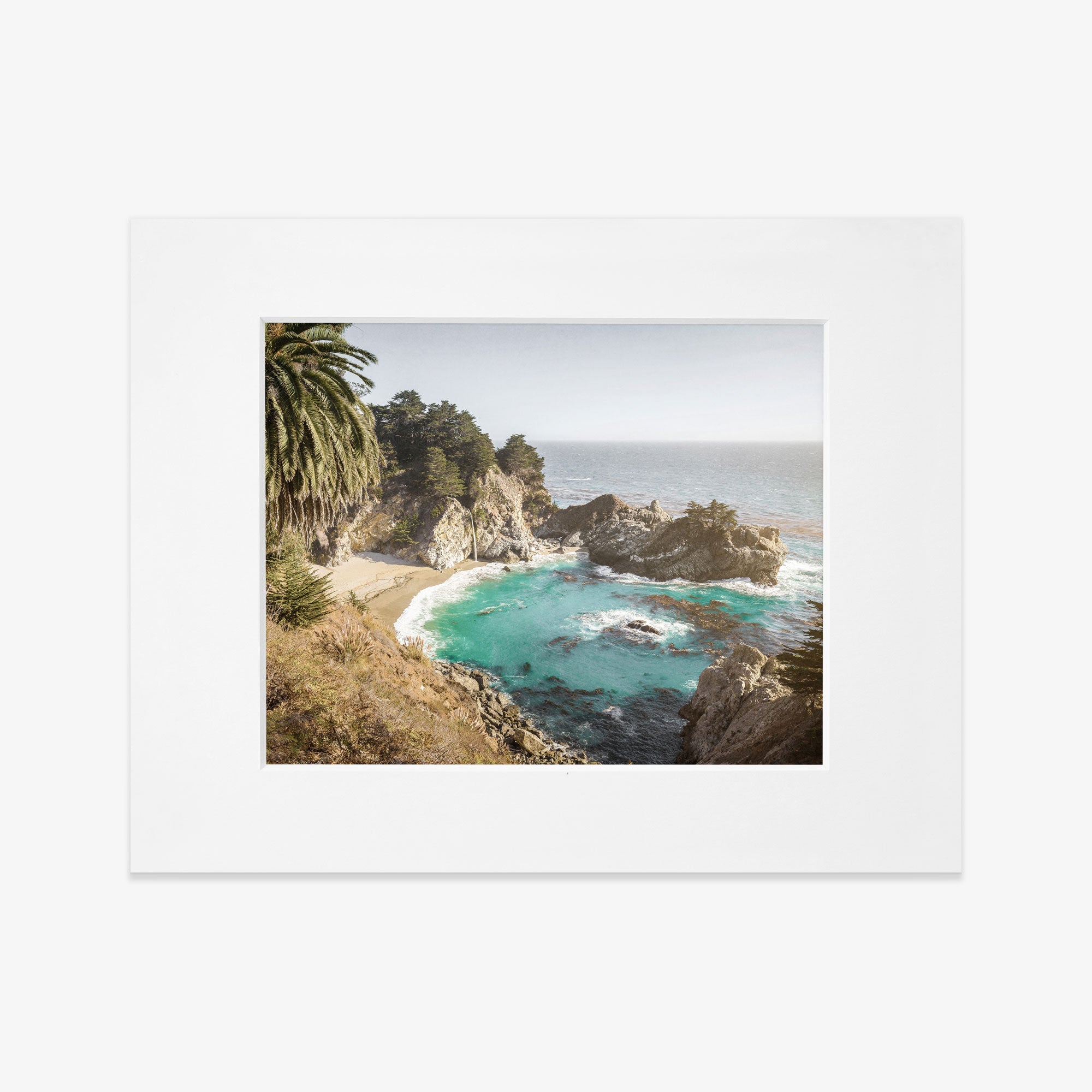 Framed photograph of a Big Sur Coastal Print, &#39;Julia Pffeifer&#39; featuring rugged cliffs along the Pacific Coast Highway, a turquoise sea, and a sandy beach flanked by green palm trees by Offley Green.