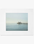 A serene image of Malibu Pier extending into a calm sea under a clear sky, framed in white, capturing a peaceful maritime scene - Offley Green's 'All Calm in Malibu' coastal print.