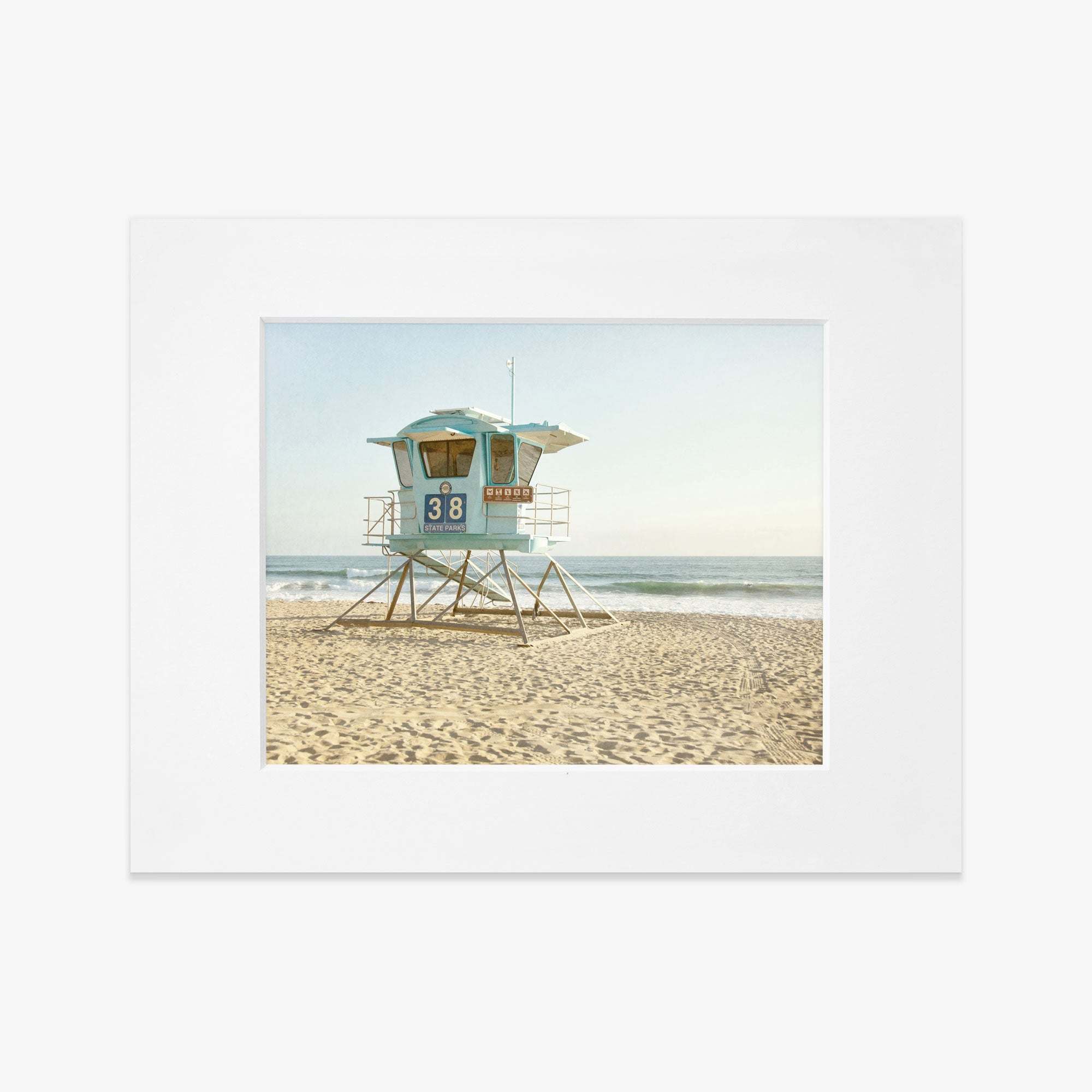 Framed photograph of a vibrant lifeguard tower numbered 38, set on a sandy beach with gentle waves in the background, under a clear blue sky on the California coastline. 
Product Name: Offley Green&#39;s California Coastal Print, &#39;Carlsbad Lifeguard Tower&#39;