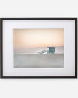 A framed photograph on white archival photographic paper depicting a Pink Coastal Print, 'Lifeguard Tower' by Offley Green on a tranquil beach at sunset, with a soft gradient sky and gentle sea.