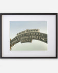 A framed archival Los Angeles California Print, 'Santa Monica Pier Blues' by Offley Green, featuring the iconic Santa Monica Pier sign with words like "sport fishing," "boating," and "cafes" against a clear sky background.