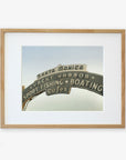 Framed archival photographic print of the Los Angeles California Print, 'Santa Monica Pier Blues' by Offley Green, featuring the iconic Santa Monica sign with text highlighting yacht harbor, sport fishing, boating, and cafes, displayed against a clear sky.