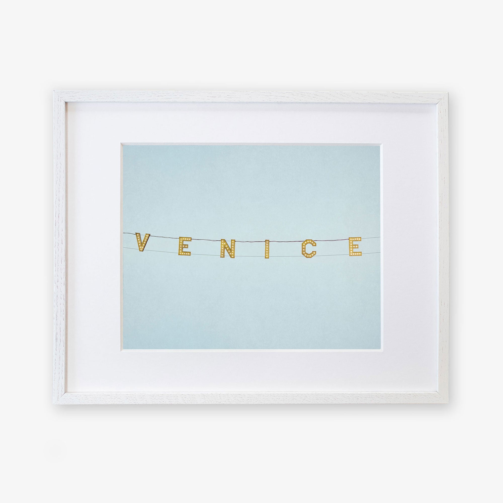 Unframed artwork featuring the Venice Beach Sign Print, 'Blue Venice' spelled out with string and small, square, gold letters against a light blue background, printed on archival photographic paper by Offley Green.
