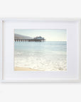Framed photograph of a peaceful beach with gentle waves lapping at the shore, showcasing 'Malibu Pier' extending into the calm blue ocean under a clear sky - Offley Green's California Beach Print.