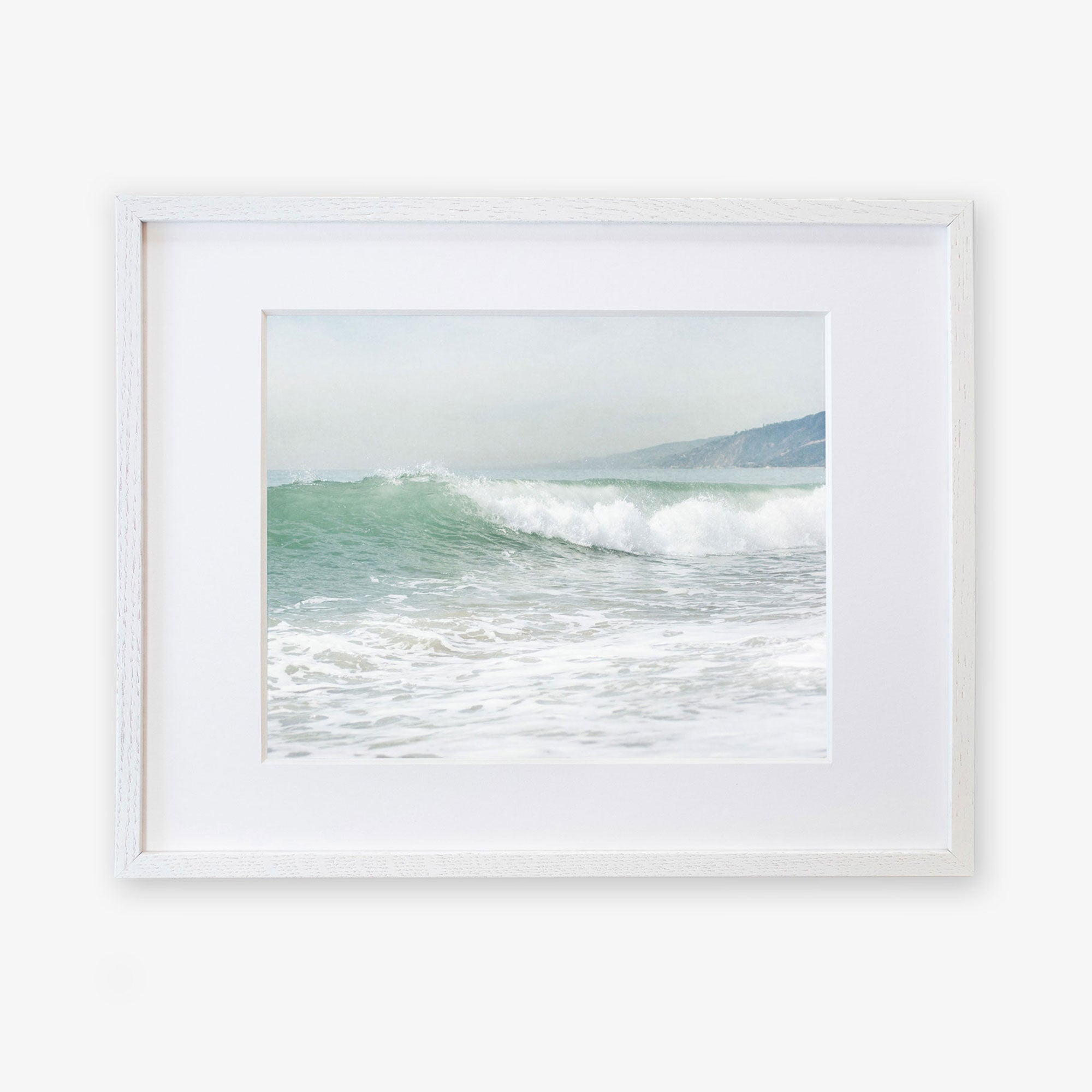 A framed Breaking Surf print of a vibrant ocean wave cresting at a Southern California beach, displayed in a simple white frame against a white background by Offley Green.