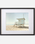 A framed Offley Green photograph depicts a lone lifeguard tower in Malibu on a sandy beach under a clear sky, creating a serene coastal scene.