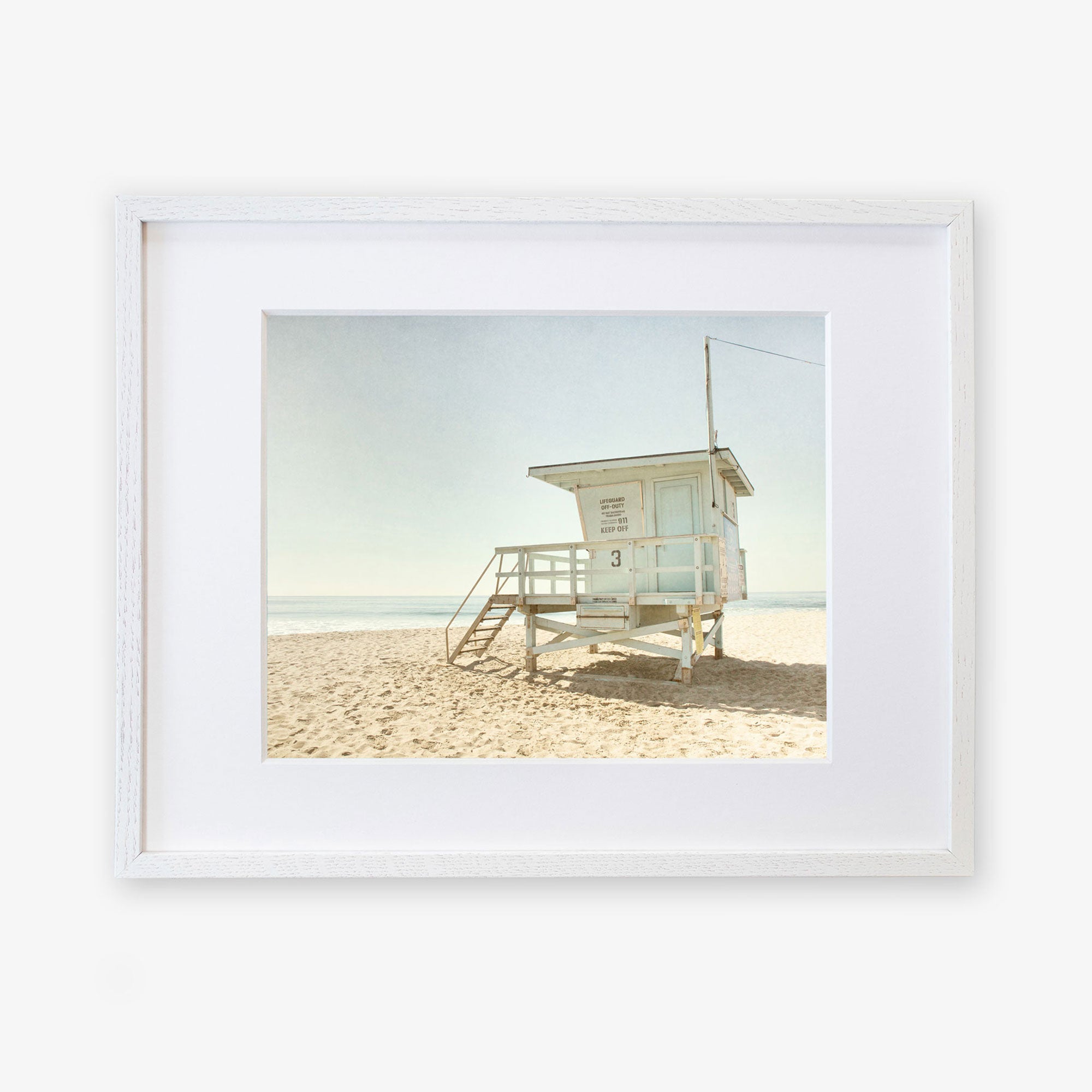 A framed photograph of &quot;California Summer Beach Art, &#39;Malibu Lifeguard Tower&#39;&quot; by Offley Green, numbered &quot;3&quot; with stairs leading up to the enclosed platform.
