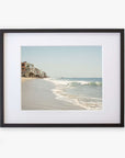 A framed photograph of a peaceful Malibu coastline showing gentle waves lapping at the shore and a row of seaside houses extending into the distance, printed on archival photographic paper by Offley Green.