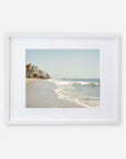 A framed Malibu Beach House Print, 'Ocean View' of a serene Malibu coastline with waves gently lapping at the shore and a row of buildings extending along the coast under a clear sky by Offley Green.