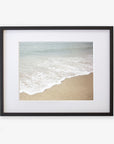 A framed Beach Waves Print, 'Chasing Surf' of a California beach scene, showing gentle waves lapping onto a sandy shore, mounted on archival photographic paper within a black frame by Offley Green.