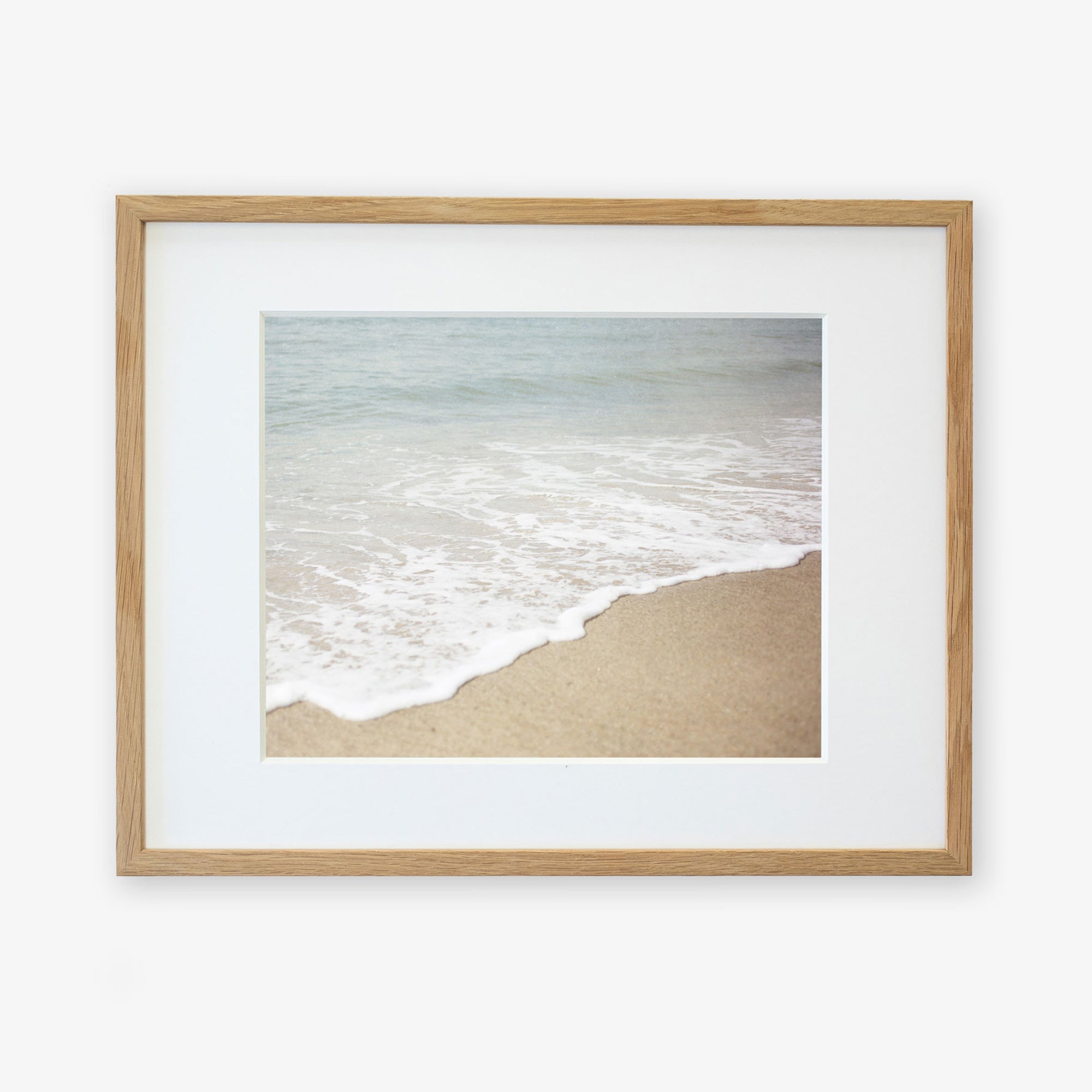 Framed photograph of a serene California beach scene showing Beach Waves Print, &#39;Chasing Surf&#39; printed on archival photographic paper and encased in a light wooden frame against a white background. Brand: Offley Green.