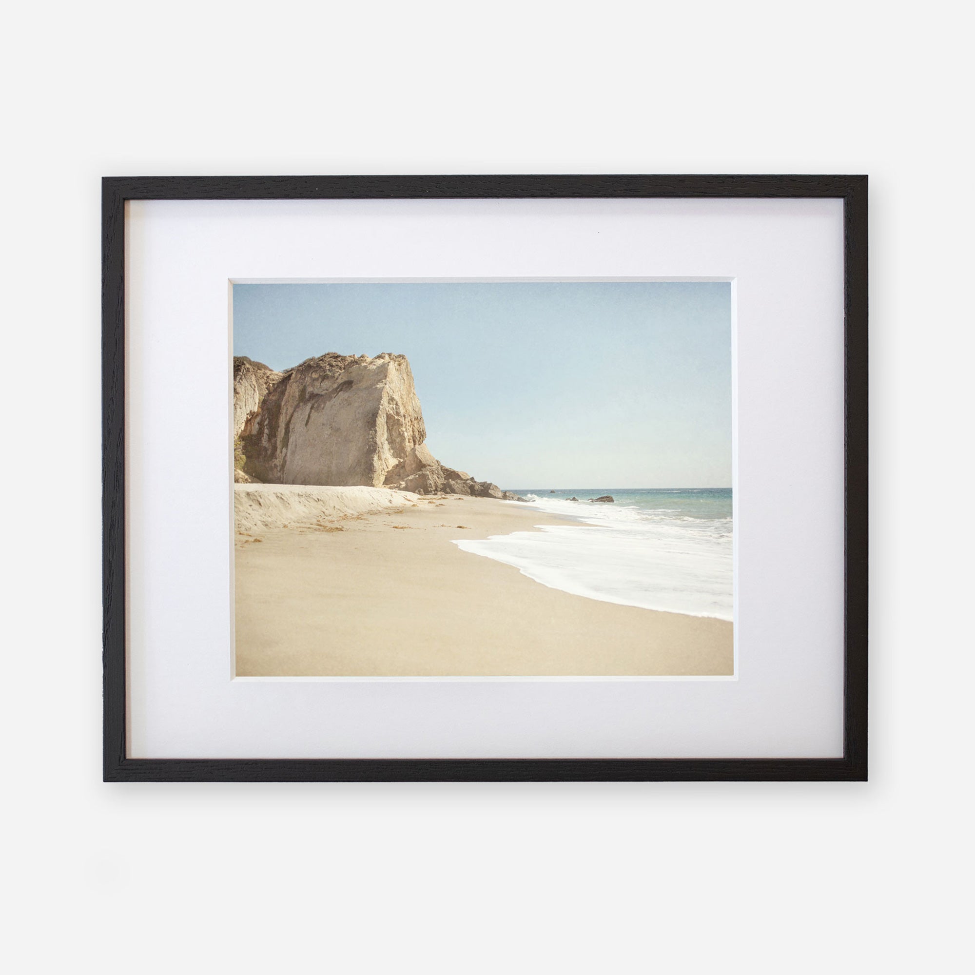 Offley Green&#39;s California Malibu Print, &#39;Point Dume&#39; featuring a serene beach scene with a sandy shore, gentle waves, and a large rock formation at Point Dume under a clear sky.