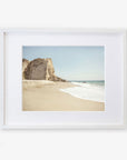 Framed photograph of a serene California Malibu Print, 'Point Dume' beach scene with a prominent rocky cliff on the left and gentle waves washing onto the sandy shore under a clear sky by Offley Green.