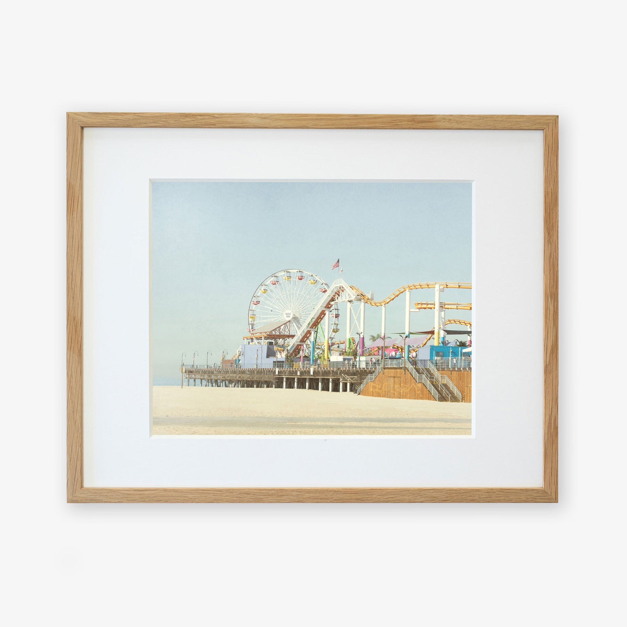 A framed illustration of a California Print, &#39;Santa Monica Pier&#39; by Offley Green, with a ferris wheel and roller coaster over Santa Monica Pier, displayed against a plain background.
