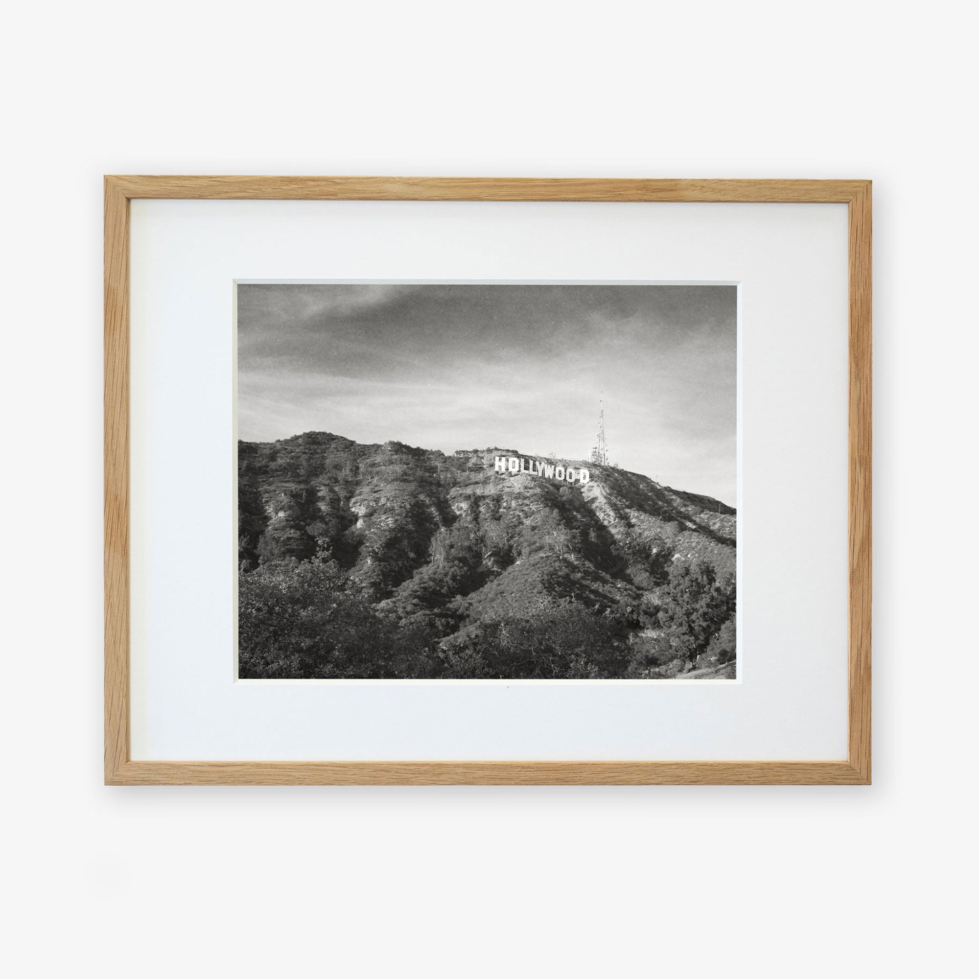 Black and white photograph of the Hollywood sign on a hill, printed on archival photographic paper, framed in a light wooden frame, against a plain white background.
Product Name: Offley Green Hollywood Sign Black and White Vintage Print, &#39;Old Hollywood&#39;