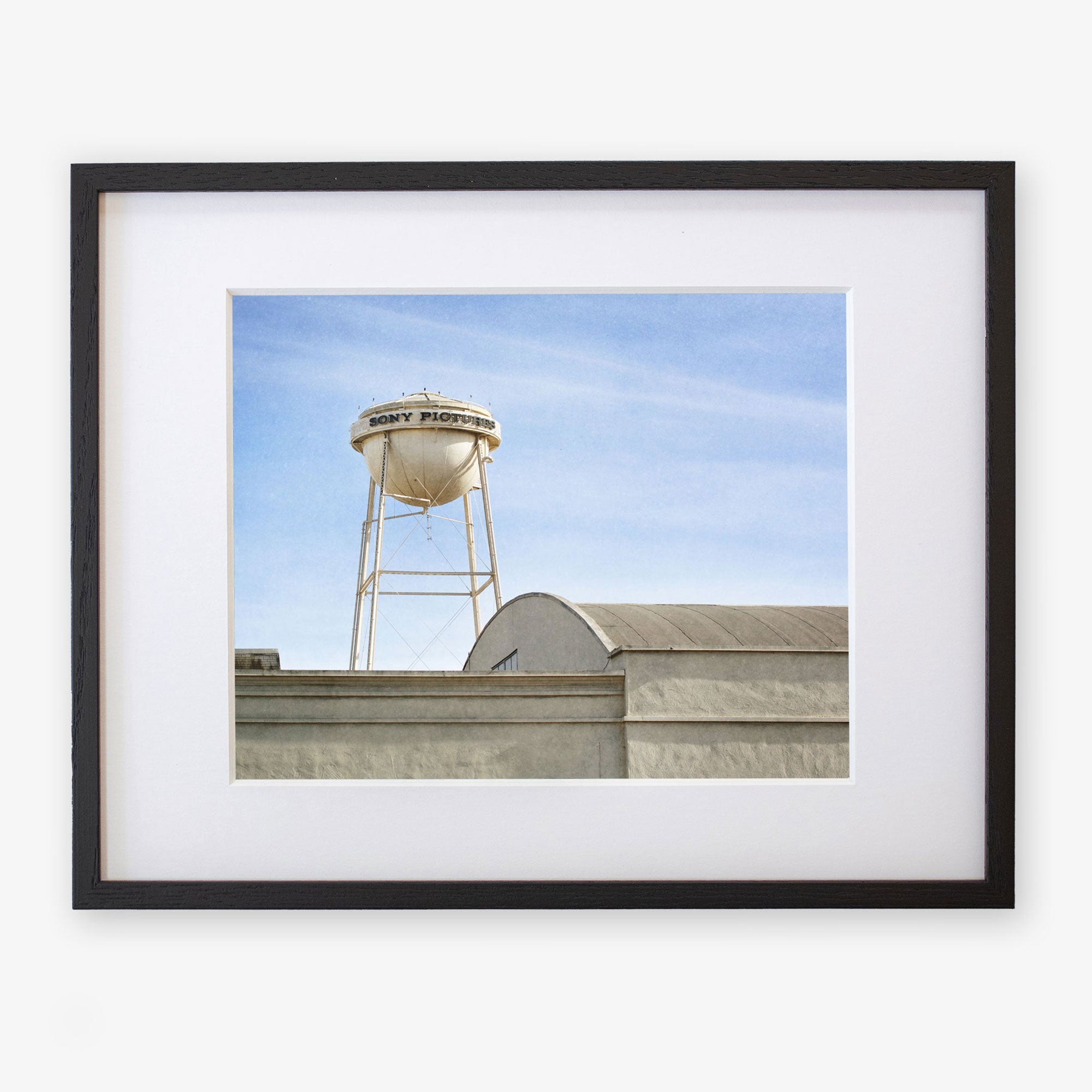A framed Offley Green photograph on archival photographic paper of an industrial scene showing a water tower labeled “city property” above warehouse roofs under a clear blue sky.
