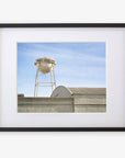 A framed Offley Green photograph on archival photographic paper of an industrial scene showing a water tower labeled “city property” above warehouse roofs under a clear blue sky.