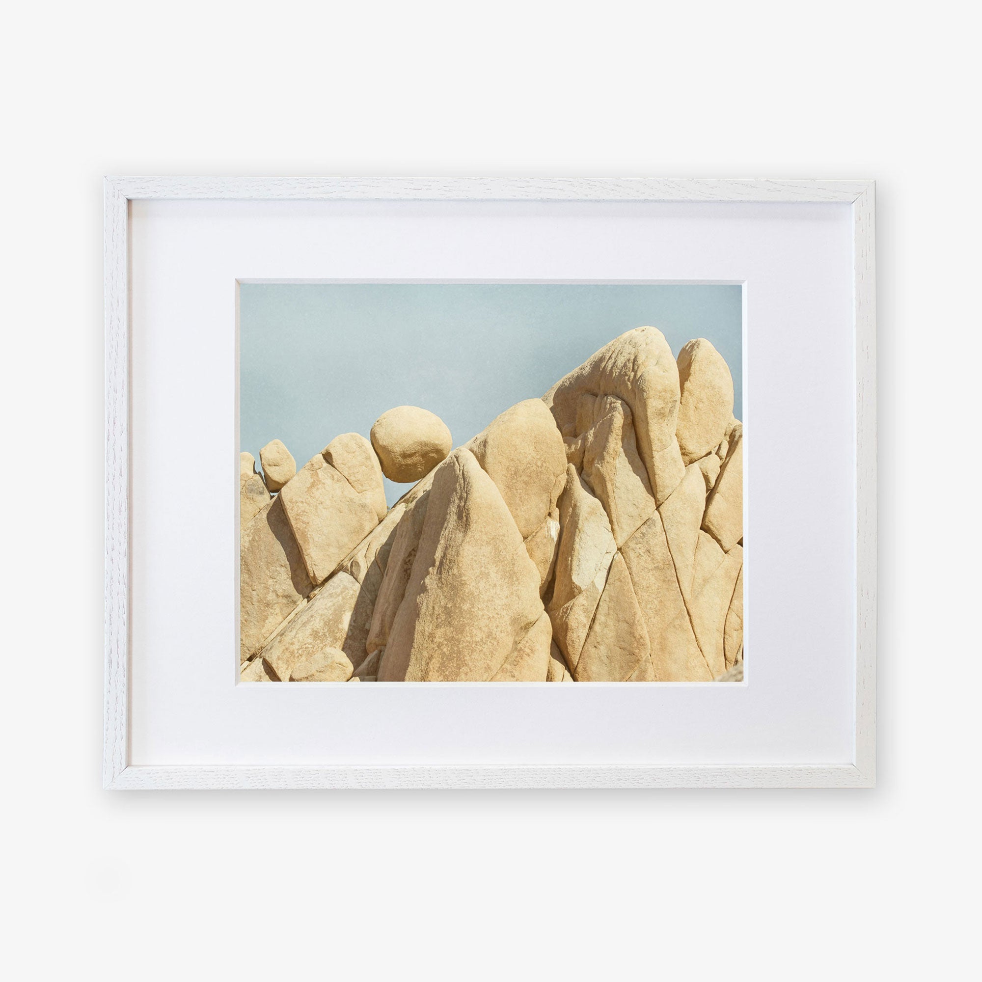 A framed photograph of jagged, beige rock formations in Joshua Tree National Park under a clear blue sky. The Offley Green frame is simple and white, highlighting the natural beauty of the geological structures.