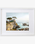 A framed painting of a California Coastal Print, 'Lone Cypress' with rugged cliffs, choppy sea, and windswept trees under a bright sky at Pebble Beach, displayed on a white background by Offley Green.