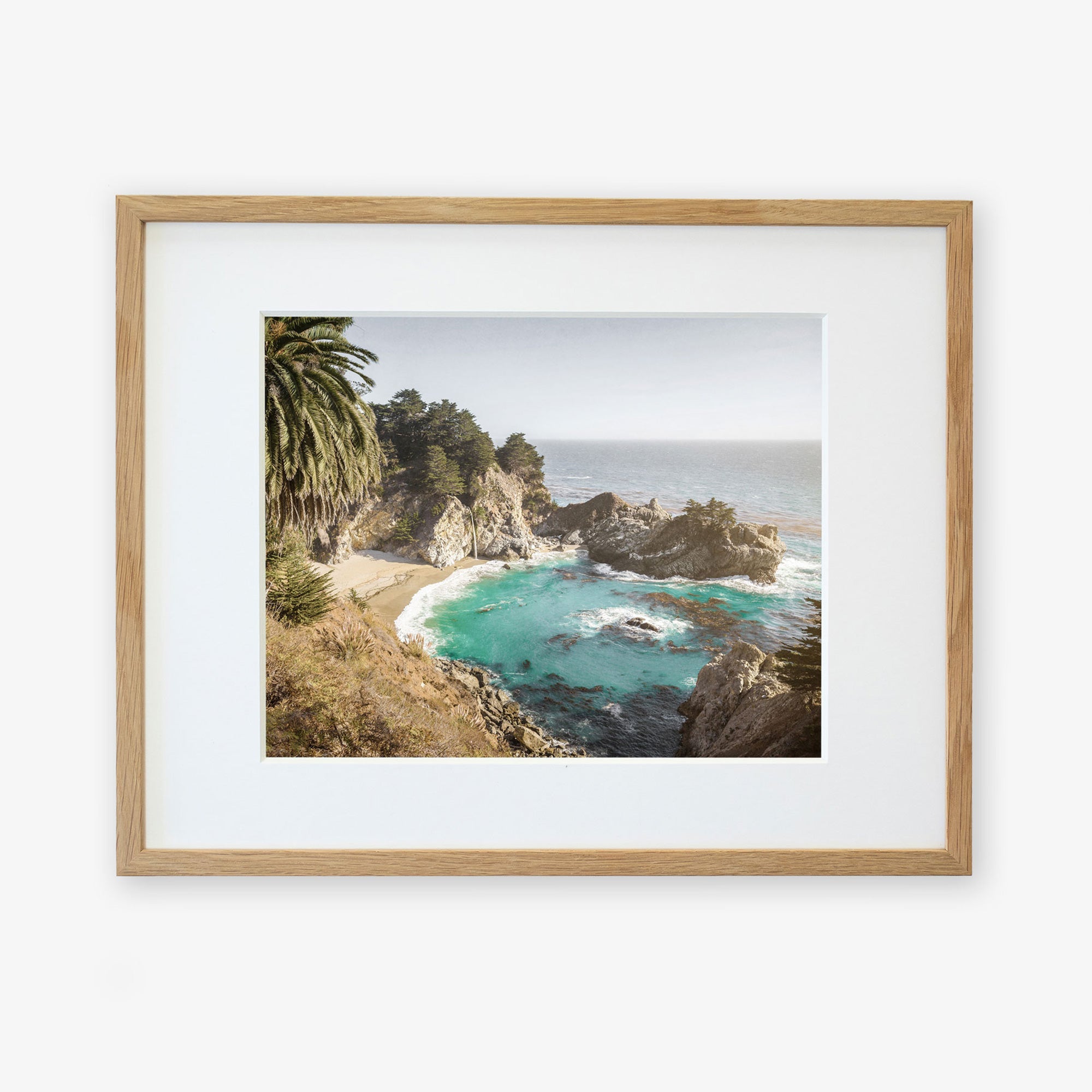 A framed photograph of a Big Sur Coastal Print, &#39;Julia Pffeifer&#39;, featuring a rocky shoreline, azure waters, and lush green foliage under a blue sky by Offley Green.
