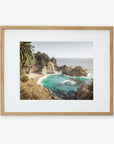 A framed photograph of a Big Sur Coastal Print, 'Julia Pffeifer', featuring a rocky shoreline, azure waters, and lush green foliage under a blue sky by Offley Green.