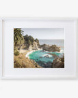 A framed artwork depicting a scenic view of the Pacific Coast Highway with turquoise waters, rocky cliffs, and lush greenery, displayed on a white background is the Big Sur Coastal Print by 'Julia Pffeifer' from Offley Green.