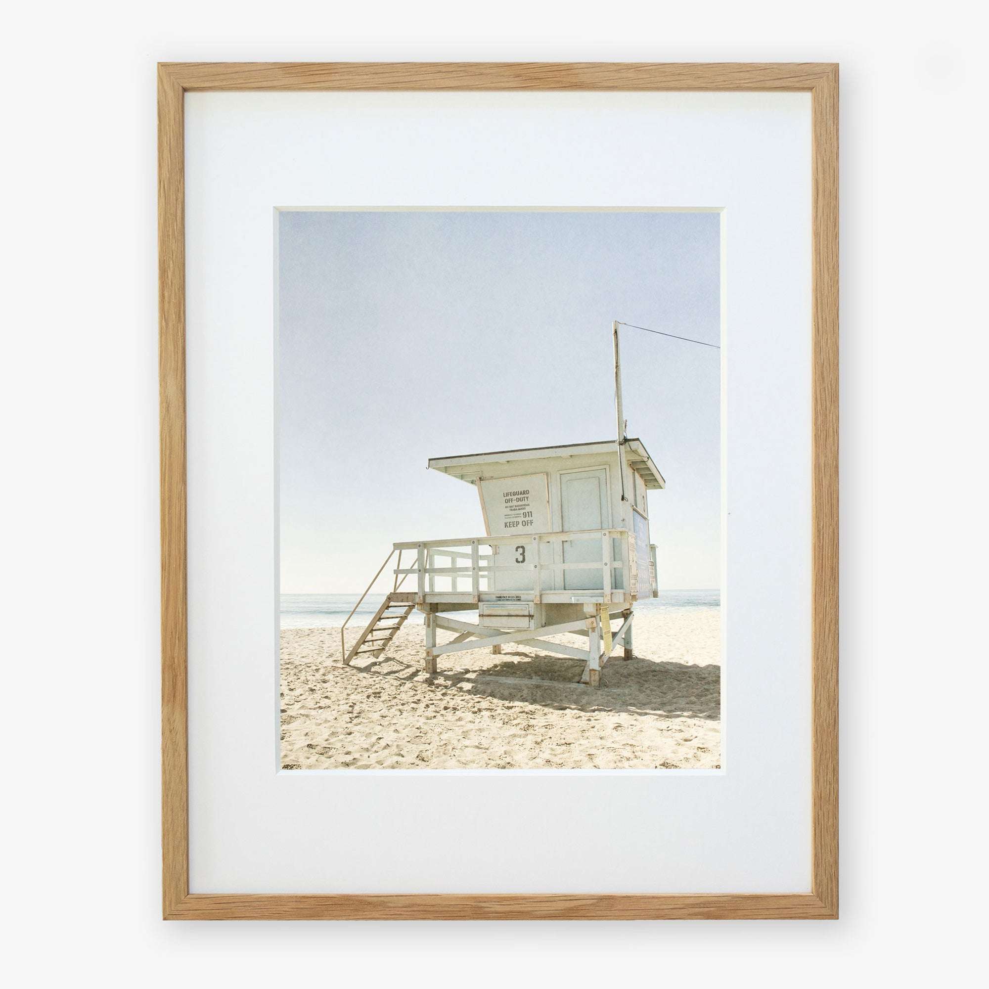 Unframed photograph of a solitary lifeguard tower on a sandy beach under a clear sky. The tower is white with steps leading up to it. California Malibu Beach Print, 'Surfrider Lifeguard' by Offley Green.
