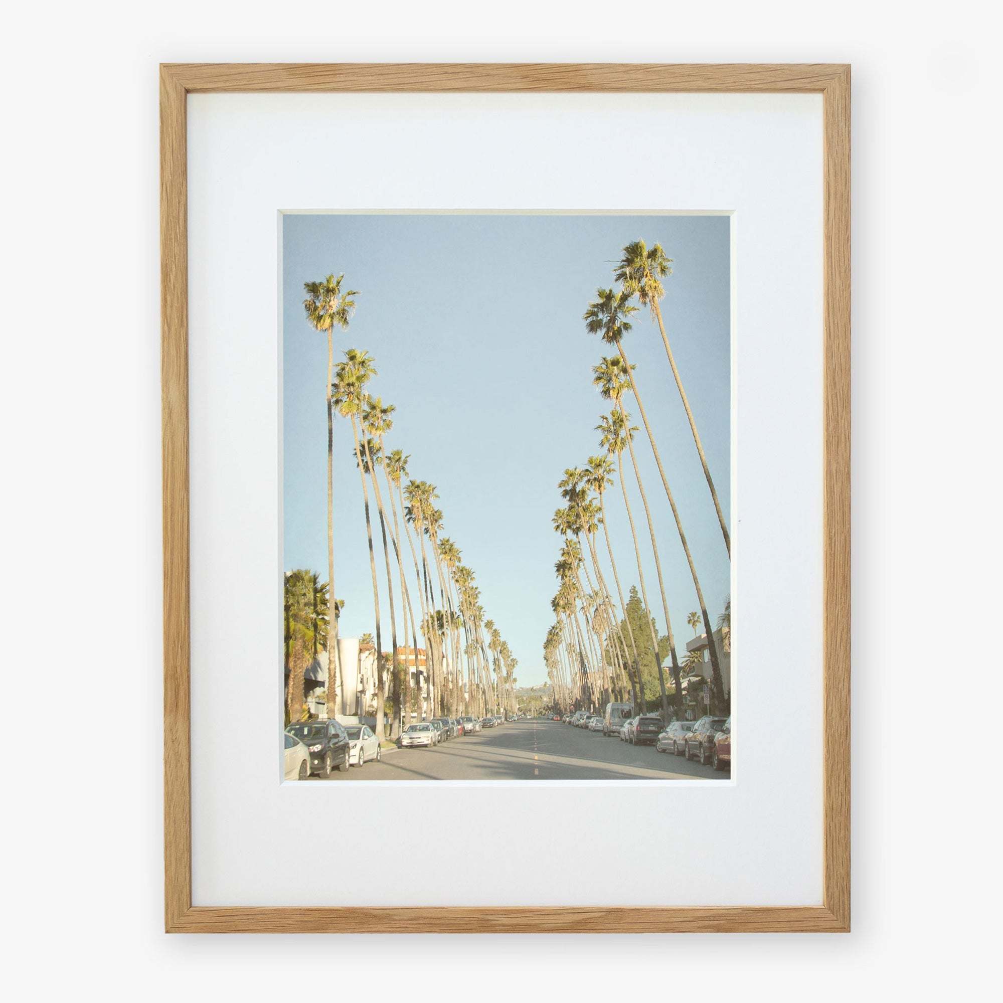 A framed photograph depicting Los Angeles Palm Tree Lined Street &#39;Sunset Boulevard Dreams&#39;, viewed from the perspective of the center of the road, under a clear blue sky by Offley Green.
