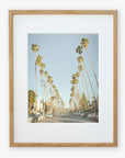 A framed photograph depicting Los Angeles Palm Tree Lined Street 'Sunset Boulevard Dreams', viewed from the perspective of the center of the road, under a clear blue sky by Offley Green.
