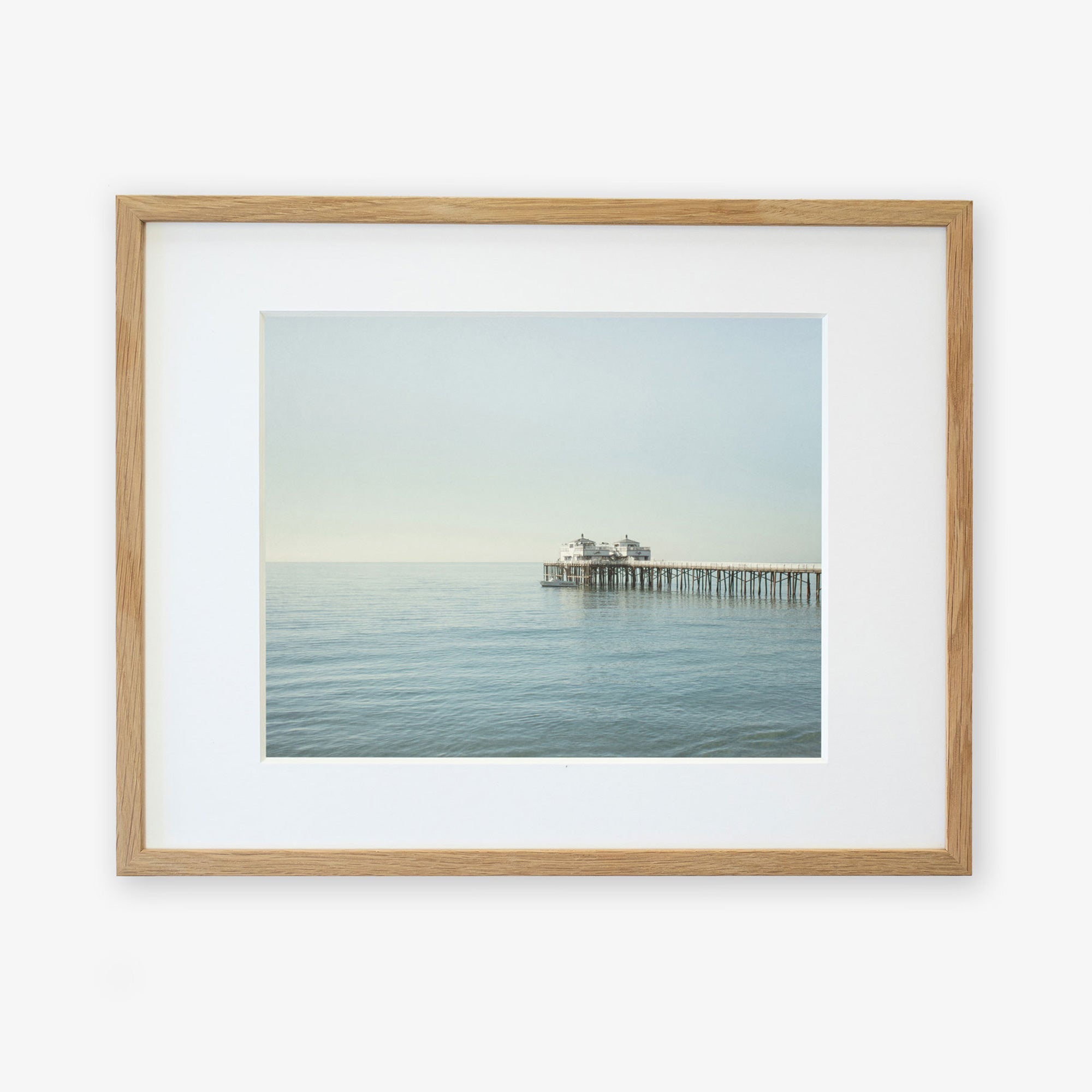 A framed photograph of Malibu Pier extending into the sea under a calm sky, displayed against a white background - Offley Green&#39;s Coastal Print of Malibu Pier in California &#39;All Calm in Malibu&#39;