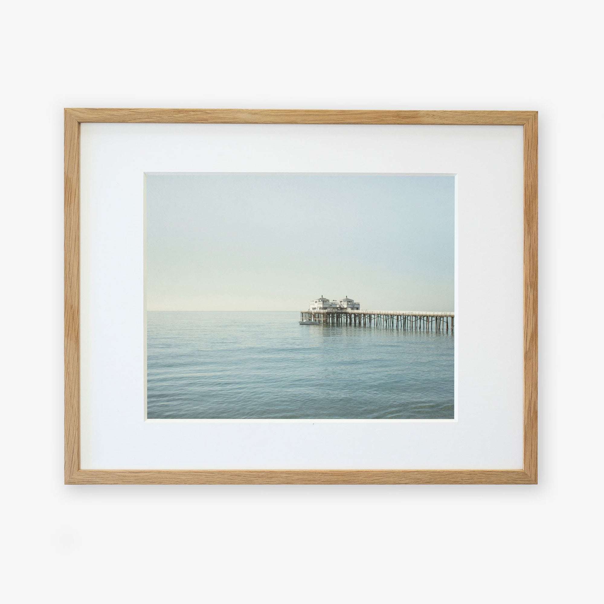 A framed photograph of Malibu Pier extending into the sea under a calm sky, displayed against a white background - Offley Green's Coastal Print of Malibu Pier in California 'All Calm in Malibu'