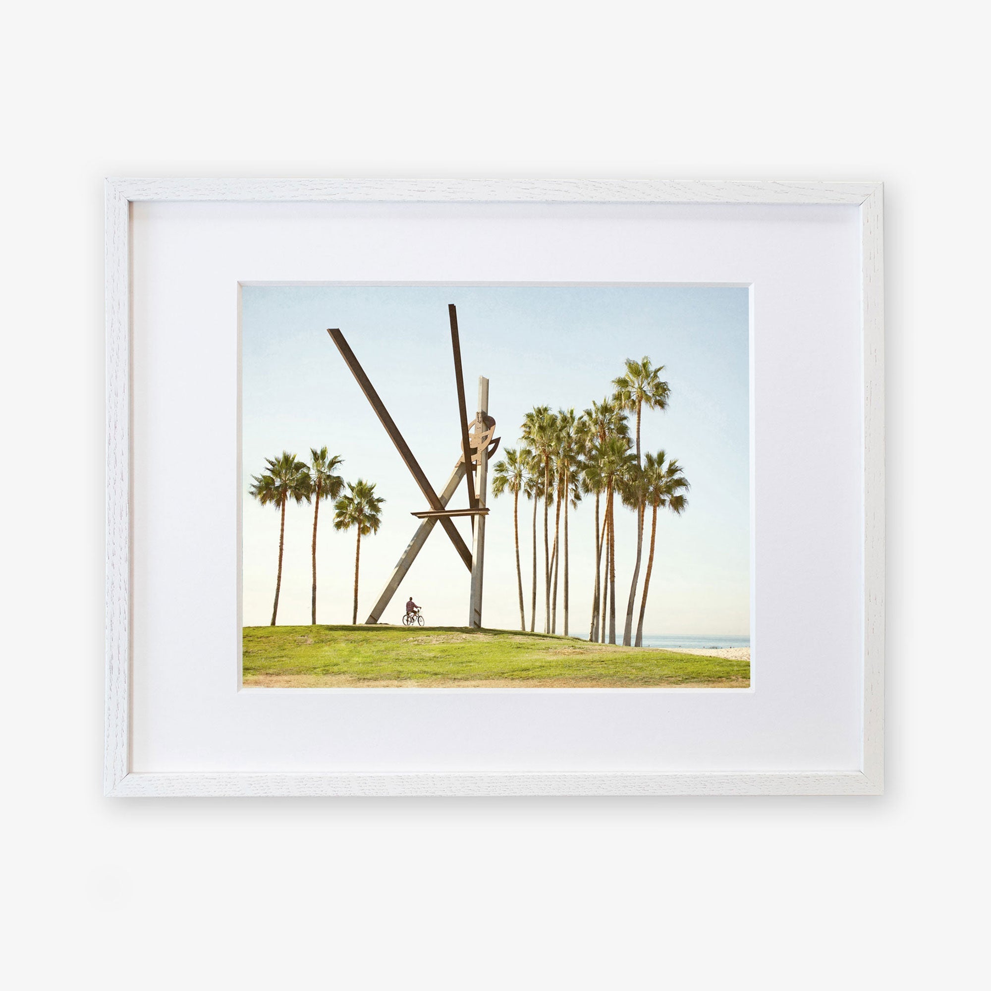 Framed artwork depicting the Venice Beach Landmark Sculpture, 'V is for Venice' by Offley Green, with large scissors cutting through the air and palm trees in the background of Venice Beach under a clear sky.