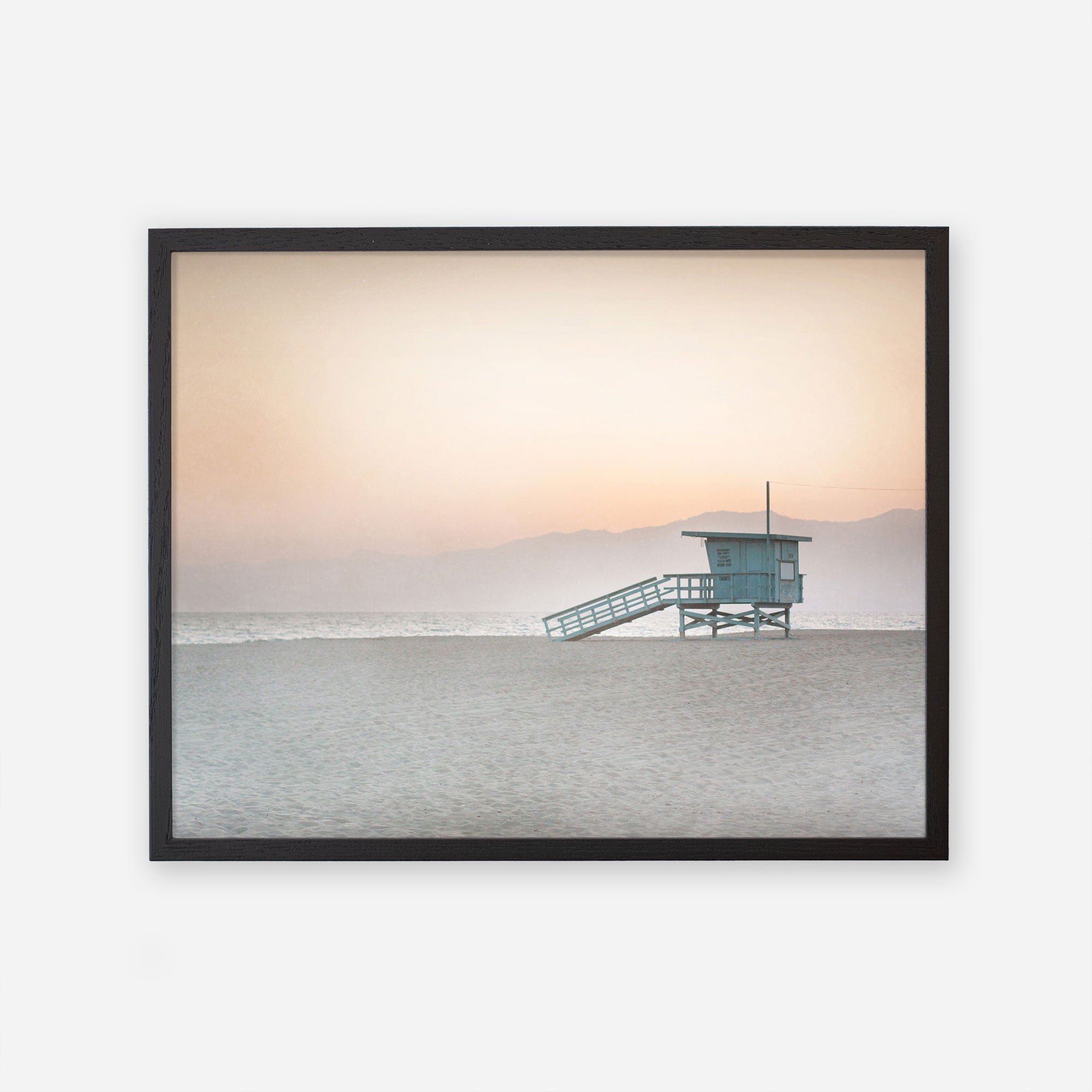 A framed photograph of a Pink Coastal Print, &#39;Lifeguard Tower&#39; by Offley Green on Venice and Santa Monica beach at sunset, with soft orange hues in the sky and calm sea waters.