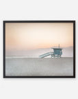 A framed photograph of a Pink Coastal Print, 'Lifeguard Tower' by Offley Green on Venice and Santa Monica beach at sunset, with soft orange hues in the sky and calm sea waters.