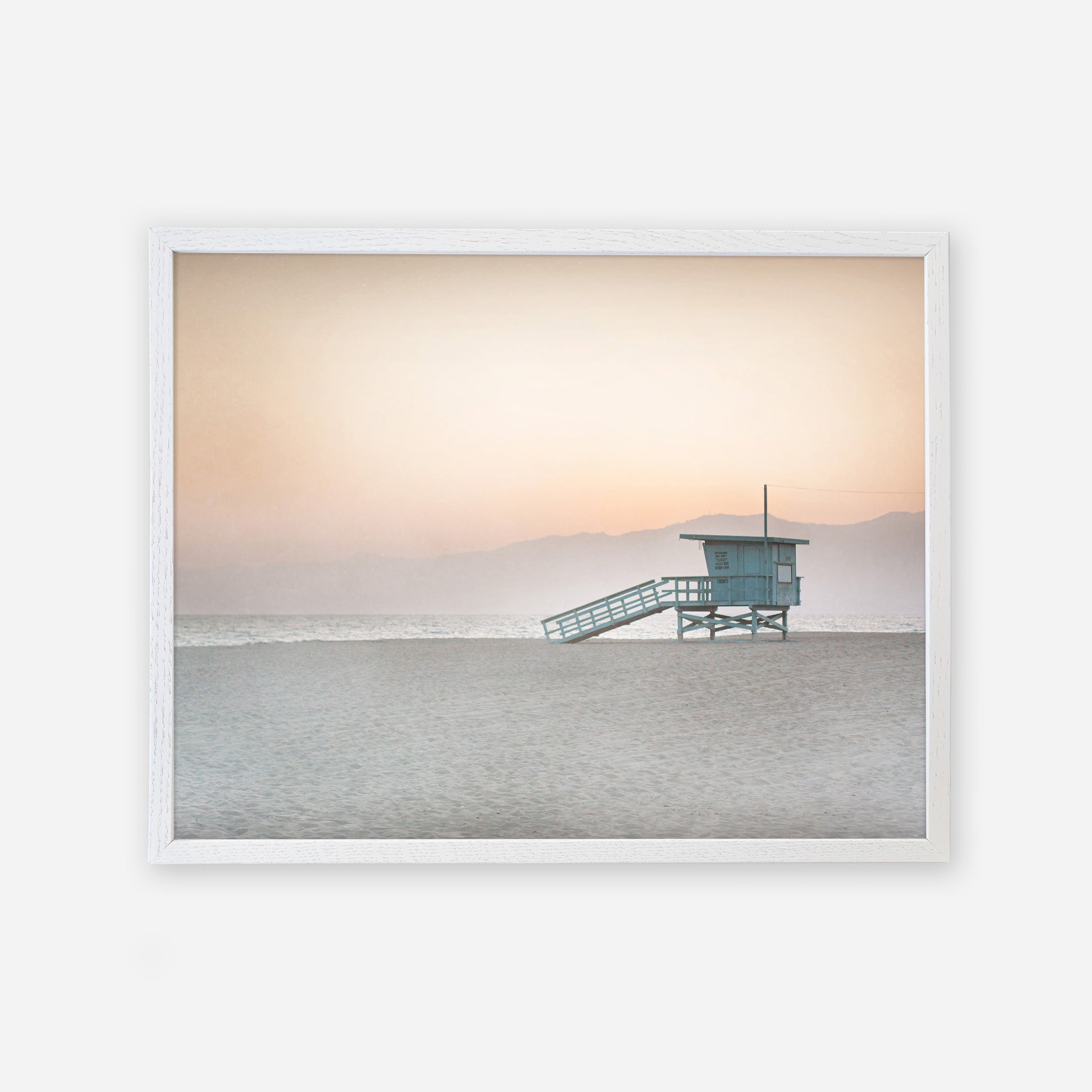 A serene Venice Beach scene with an Offley Green &#39;Pink Coastal Print, Lifeguard Tower&#39; centered in the frame, set against a soft pink sunset and hazy mountain backdrop.