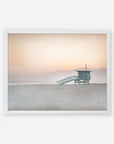 A serene Venice Beach scene with an Offley Green 'Pink Coastal Print, Lifeguard Tower' centered in the frame, set against a soft pink sunset and hazy mountain backdrop.