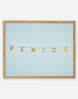 A light blue bulletin board displaying a decorative string with letters spelling "Venice Beach Sign Print, 'Blue Venice'" in a horizontal arrangement, each letter on a separate, small flag by Offley Green.