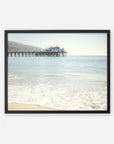 A framed photograph of a serene beach scene, showcasing gentle waves washing ashore with Malibu Pier extending into the ocean, topped by a small building under a clear sky. Offley Green's California Beach Print featuring 'Malibu Pier'.