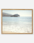 A framed photograph of a tranquil beach scene with gentle waves lapping at the shore and 'Malibu Pier' extending into the ocean, supporting a large building under a clear sky. This is the Offley Green California Beach Print.