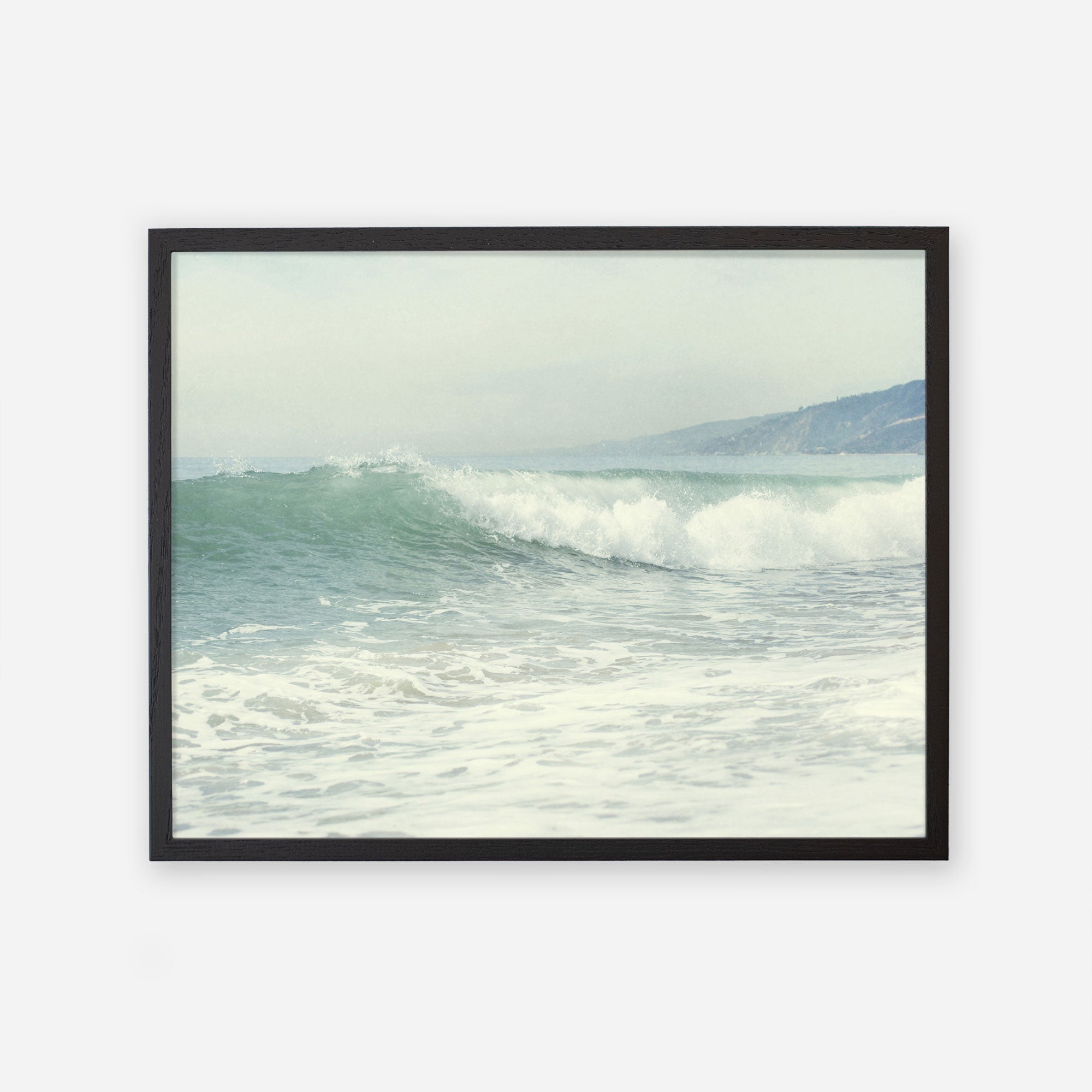 A framed Offley Green Coastal Print of a Breaking Wave &#39;Breaking Surf&#39;, depicting a gentle wave cresting in the ocean with hazy hills visible in the background. The image, printed on archival photographic paper, evokes a serene Southern California beach scene.