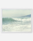 A framed illustration of gentle ocean waves rolling onto a Southern California beach, with hazy hills visible in the background under a soft, pale sky featuring the Offley Green Coastal Print of a Breaking Wave 'Breaking Surf'.