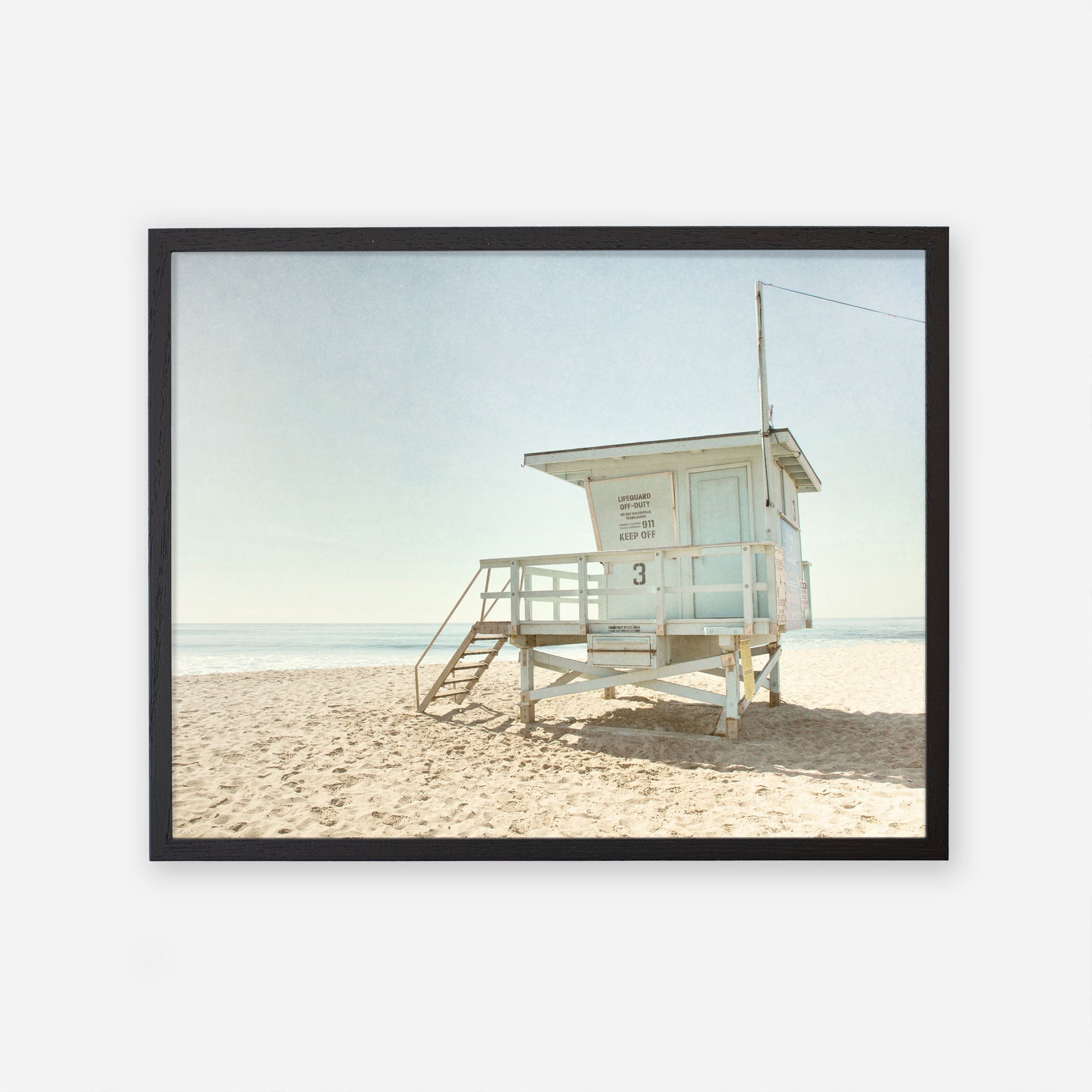 A framed photograph of the California Summer Beach Art, &#39;Malibu Lifeguard Tower&#39; by Offley Green, situated on a sandy beach in Malibu under a clear sky, with its facade numbered &quot;3&quot;.