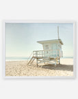 A framed picture of California Summer Beach Art, 'Malibu Lifeguard Tower' by Offley Green on a serene beach under a clear sky. The sandy beach is empty, emphasizing the calmness of the setting.
