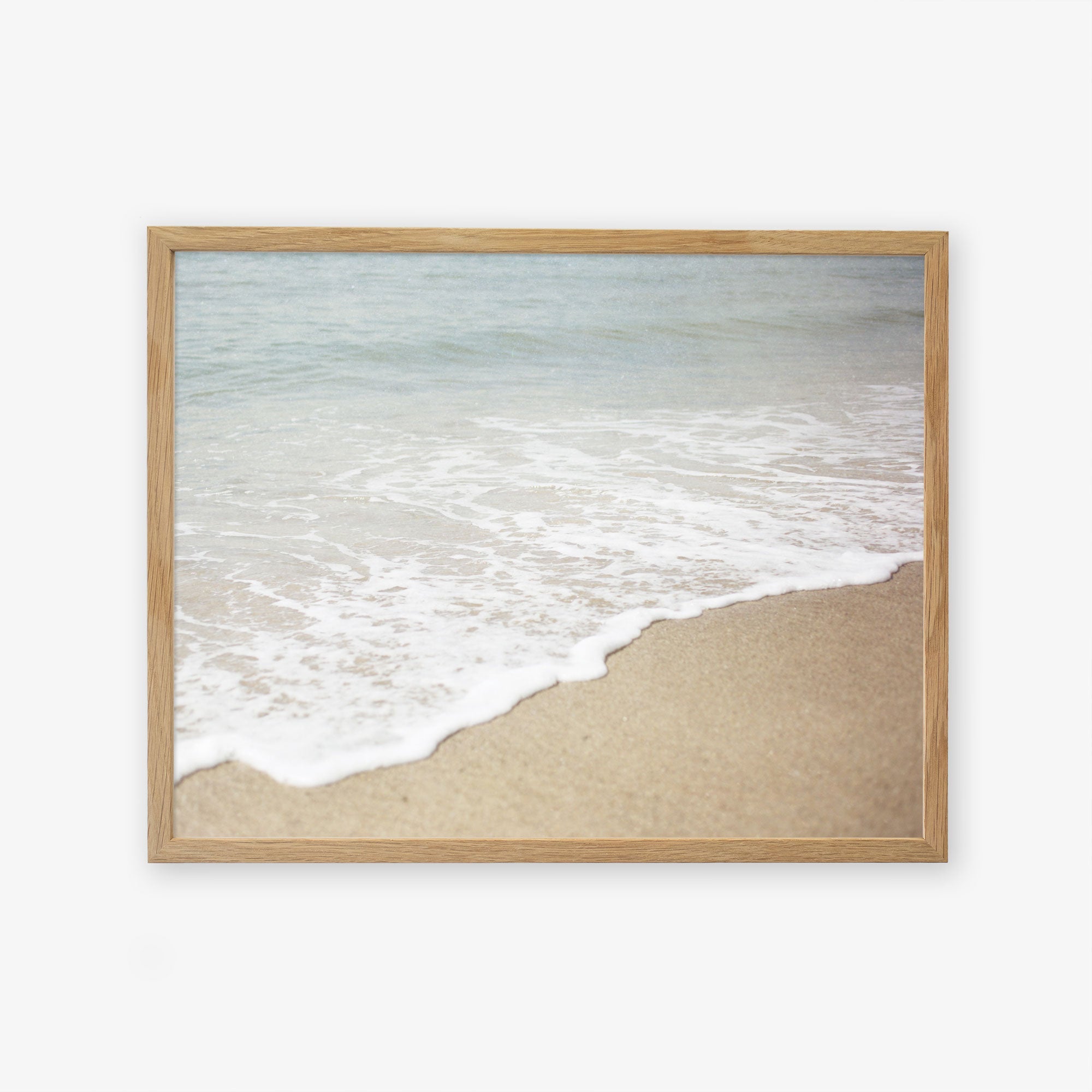 A framed photograph of Offley Green&#39;s &#39;Chasing Surf&#39; Beach Waves Print, capturing the gentle waves meeting the sandy shore in a serene California beach scene, displayed on a plain white background.