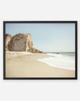 A framed photograph depicting a serene beach scene at Point Dume with a large cliff on the left, gentle waves washing onto the sandy shore, and a clear blue sky - Offley Green's California Malibu Print, 'Point Dume'