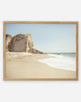 A framed painting of a serene beach scene at Point Dume, with a large cliff on the left, white sand, and gentle waves under a clear sky by Offley Green's California Malibu Print, 'Point Dume'.