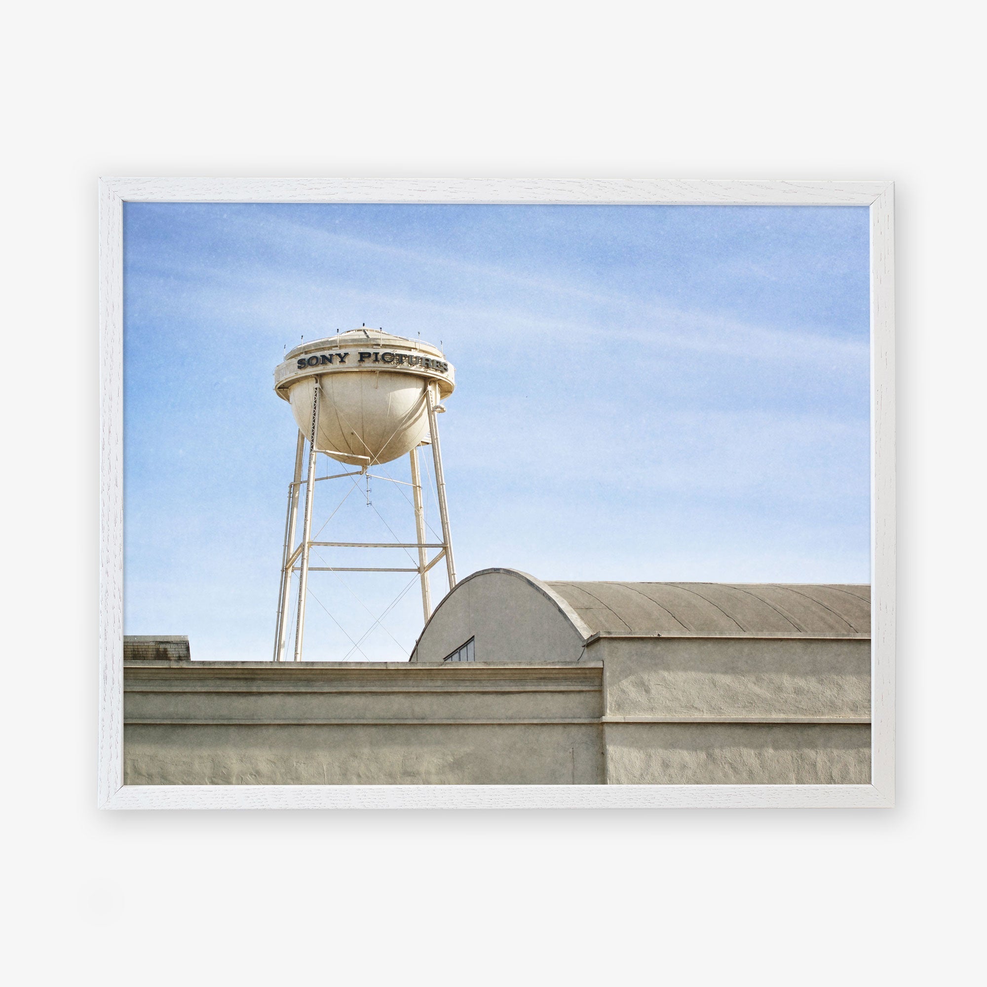 A water tower labeled &quot;Offley Green Studios&quot; stands above a building under a clear blue sky. The tower and the building&#39;s roof are framed in a white border.