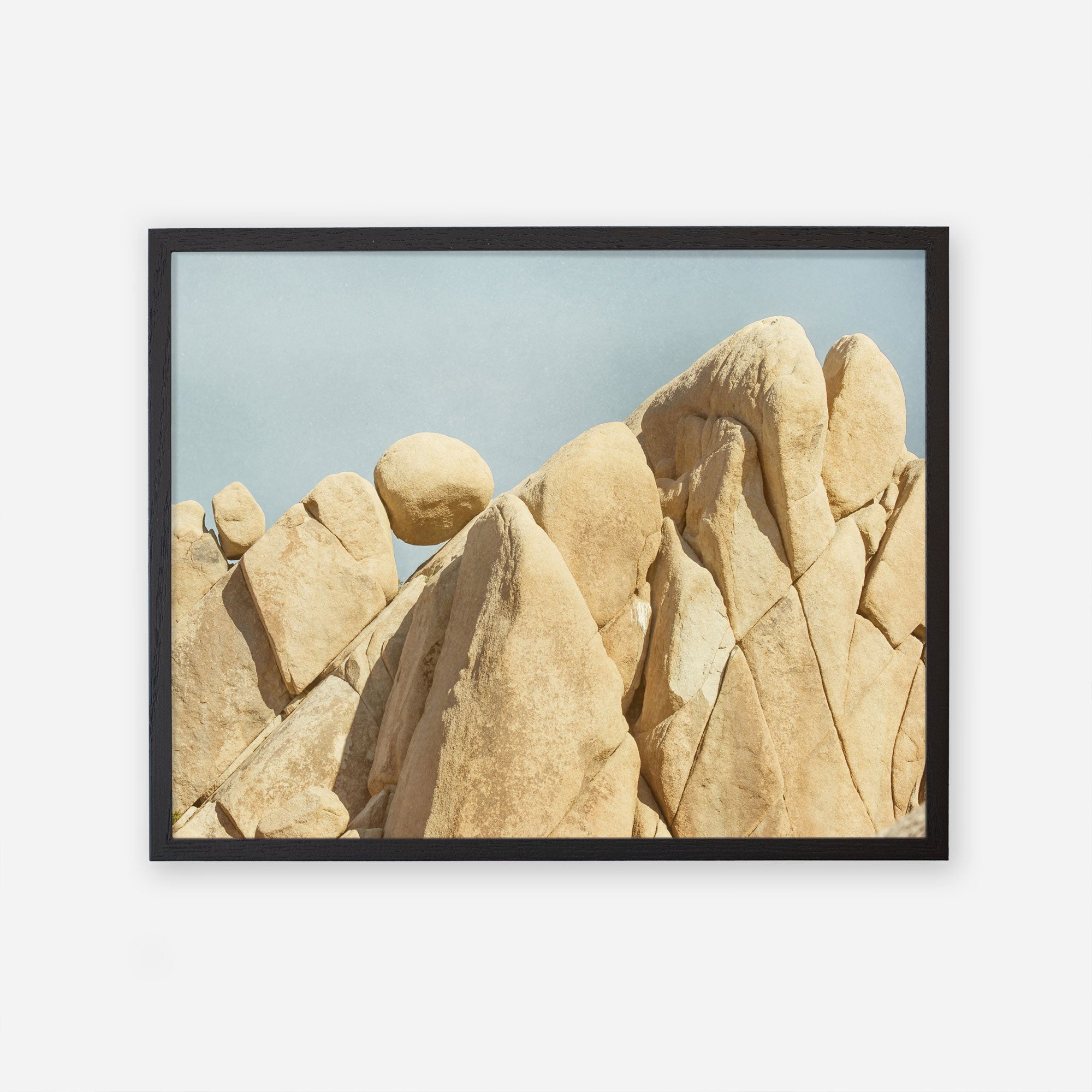 A framed photograph of rugged desert rock formations in Joshua Tree National Park under a clear blue sky, showcasing warm beige tones and smooth, windswept textures by Offley Green.